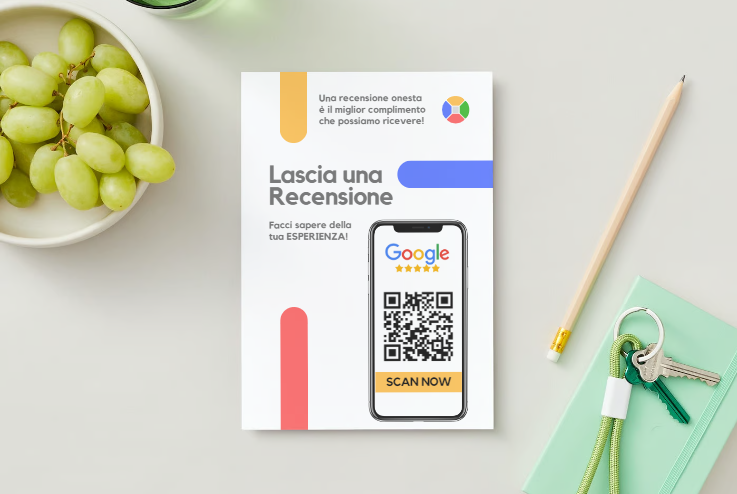 Un volantino con informazioni su come lasciare una recensione su Google, esposto su una scrivania con una ciotola di uva, chiavi, una pianta e un quaderno verde. Il volantino include un codice QR da scansionare.
